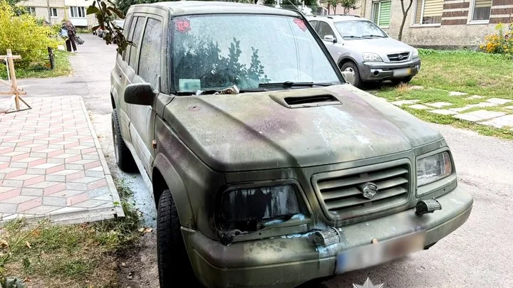 Брудний оливковий Suzuki з пошкодженим бампером біля багатоповерхівки